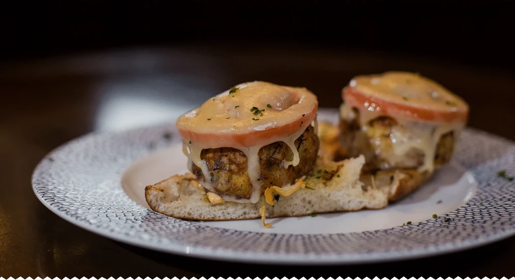Two open-faced sandwiches with patties, melted cheese, tomato, and herbs.