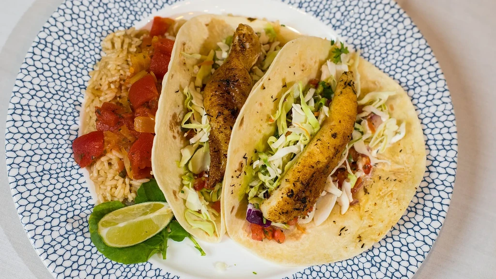 Two fish tacos, rice with stewed tomatoes, and a lime.