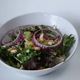 Fresh salad with mixed greens, red onion, white cheese, and nuts.