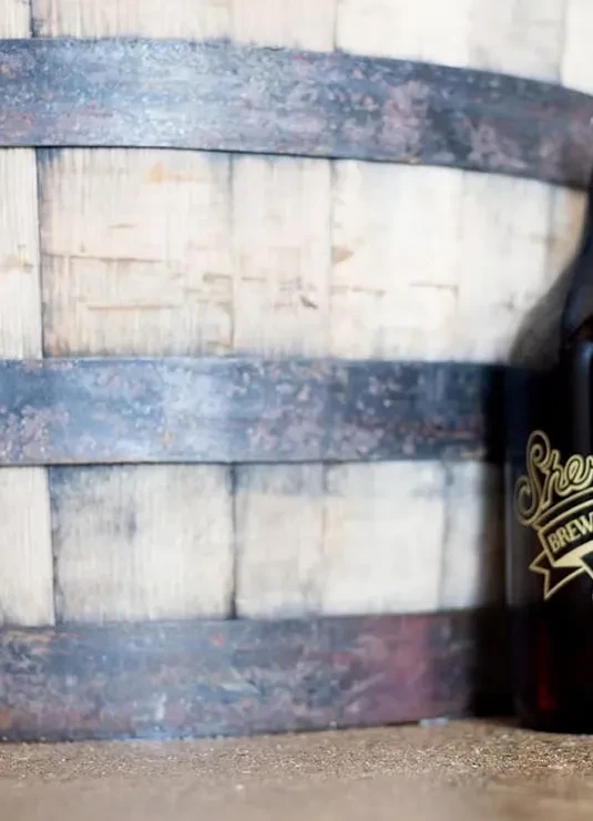 Close-up of a rustic wooden barrel and a labeled beer bottle.