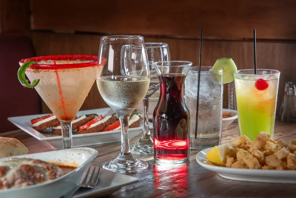 Close-up of a table laden with cocktails, wine, pasta, and calamari.