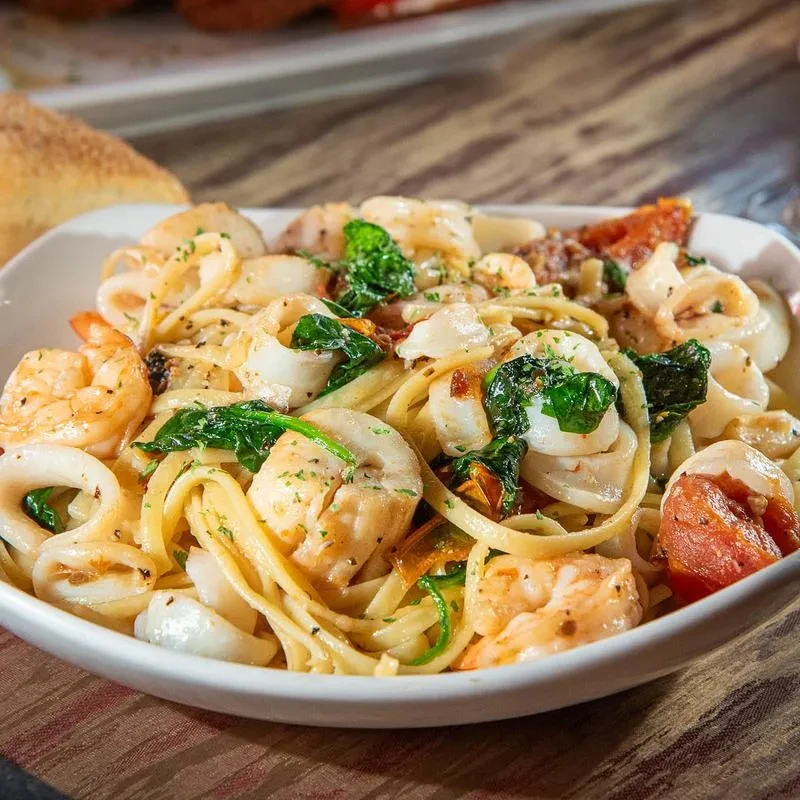 Linguine with shrimp, scallops, calamari, spinach in a white bowl.
