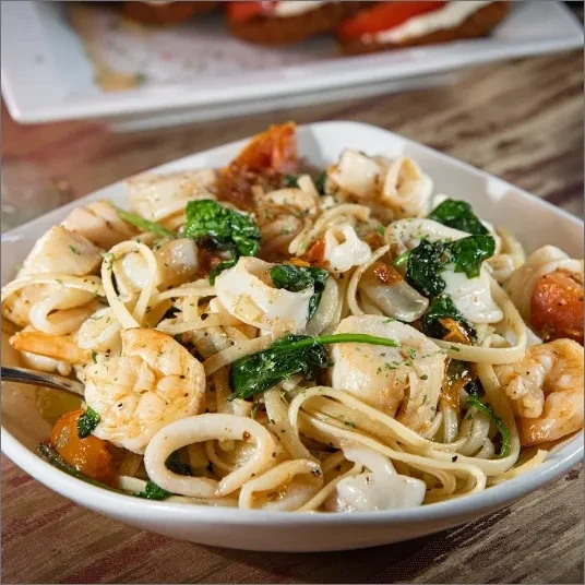 White bowl of linguine pasta with shrimp, calamari, scallops, and spinach.