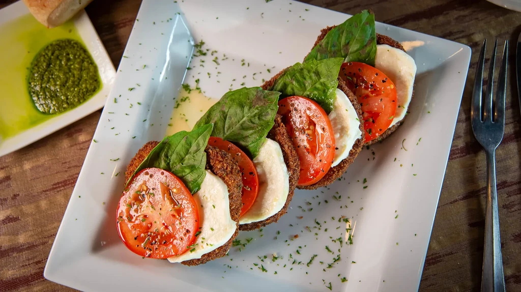 Five dark-based appetizers with tomato, mozzarella, and basil.