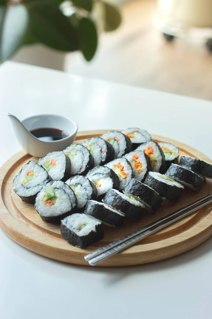 Fresh maki sushi rolls, soy sauce, and chopsticks on a wooden board.