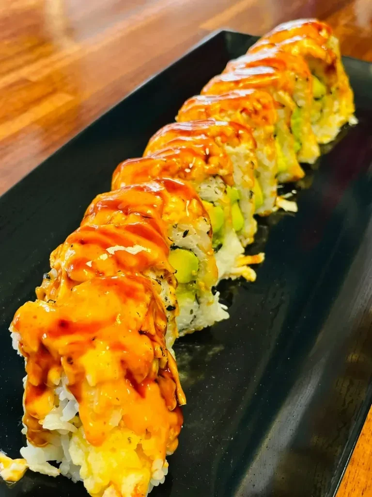 Sushi roll pieces with avocado and orange-red sauce on a black plate.
