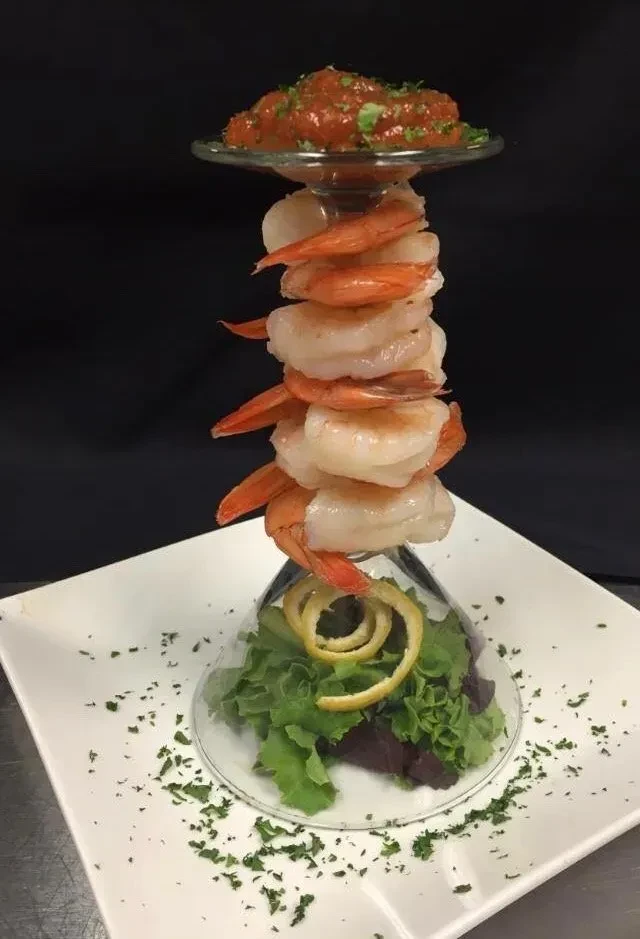 Shrimp cocktail with shrimp stacked around inverted glass, sauce, and lettuce.