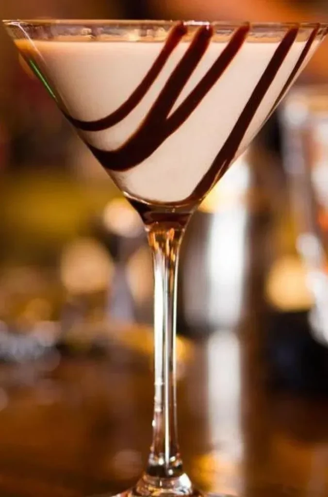 Creamy drink in a chocolate-swirled martini glass with bokeh lights.