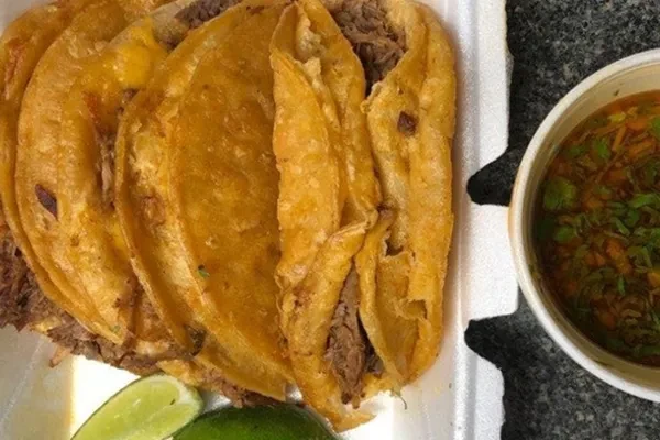 Crispy birria tacos with consommé and lime in a takeout container.