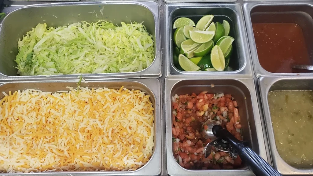 Overhead view: six containers of fresh Mexican buffet toppings.