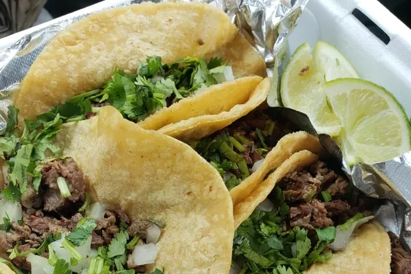 Three carne asada tacos with cilantro, onions, and lime wedges.