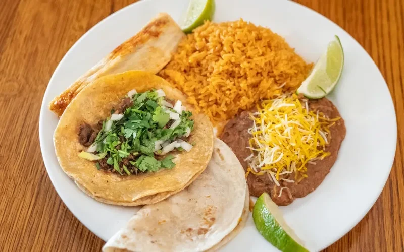 Plate of carne asada tacos, Mexican rice, and cheesy refried beans.