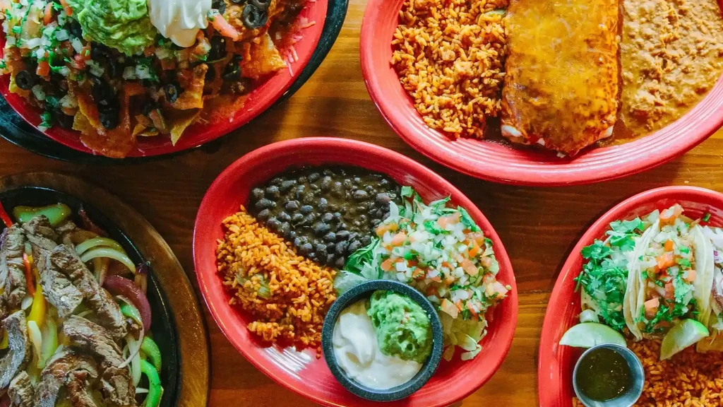 Multiple vibrant Mexican and Tex-Mex dishes on a wooden table.