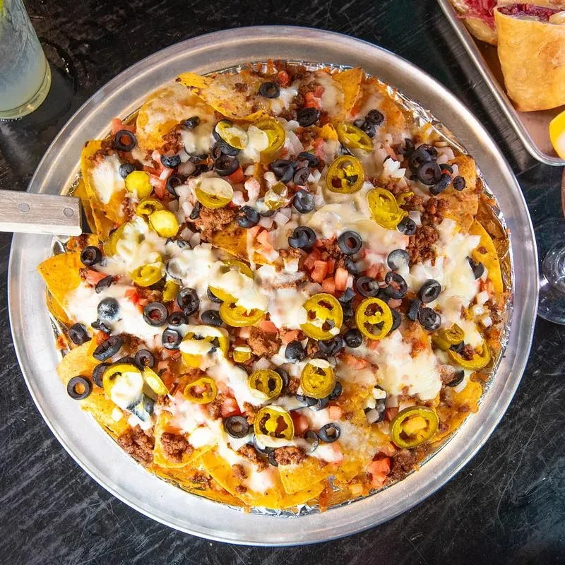 Top-down view of large nachos with cheese, meat, jalapeños, olives, tomatoes.