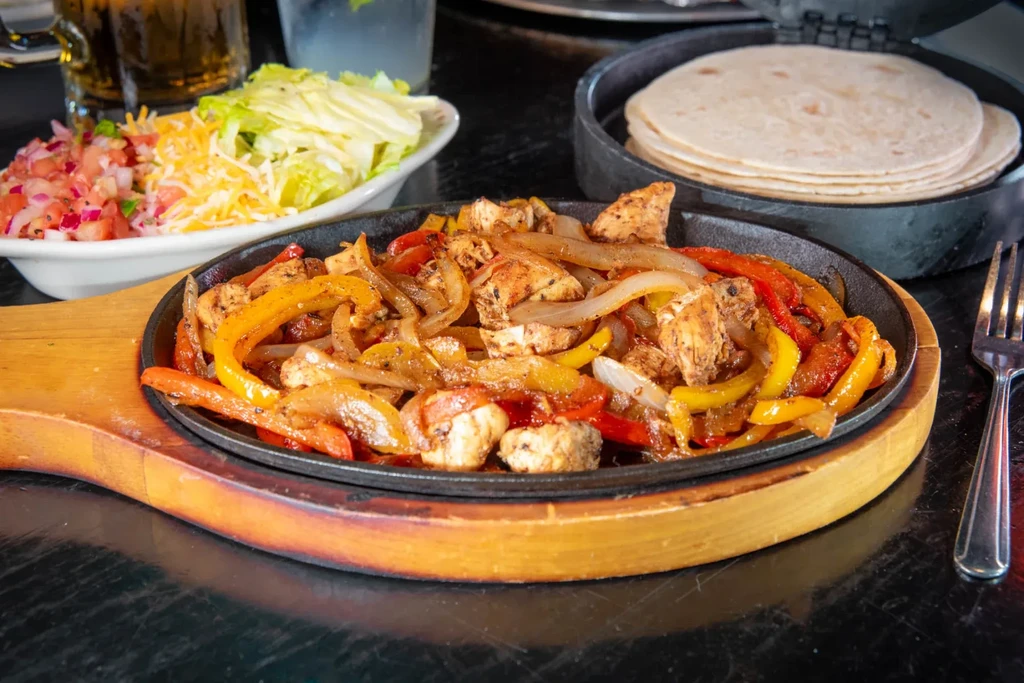 Sizzling chicken fajitas with peppers, onions, salsa, and tortillas.