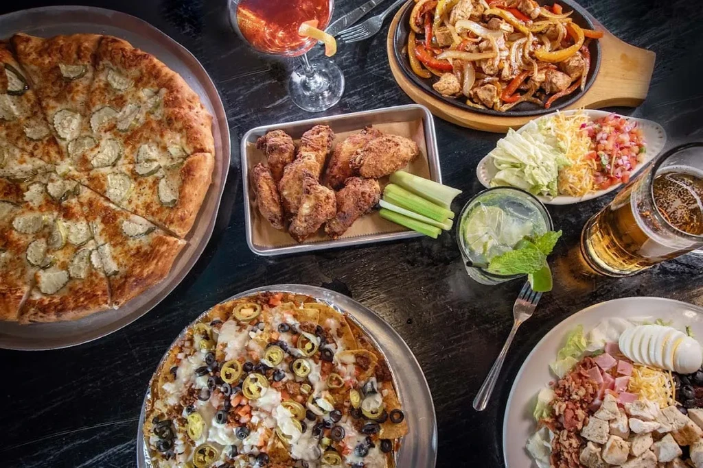 Pizza, fajitas, nachos, wings, salad, and various drinks on a table.