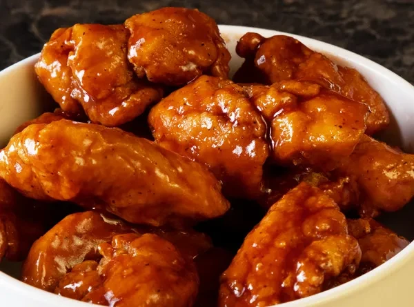 Bowl of glossy reddish-orange glazed chicken pieces.