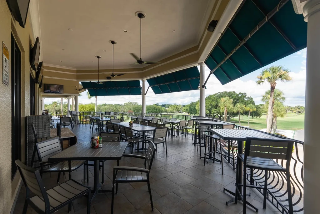 Covered patio with dark furniture, golf course view, teal awnings.