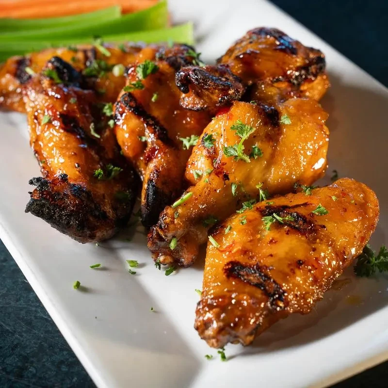 Crispy glazed chicken wings with char marks and herbs on a white plate.