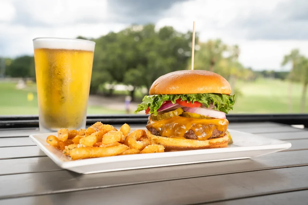Gourmet cheeseburger, seasoned fries, and frosty beer served outdoors.
