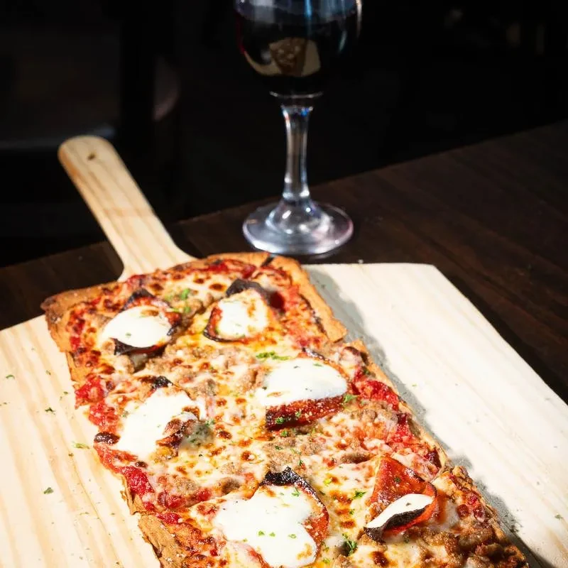 Rectangular pizza with meat, melted and fresh mozzarella, and herbs on a peel.