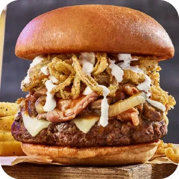 Gourmet beef burger with melted cheese, bacon, fried onion strings, and onion rings.