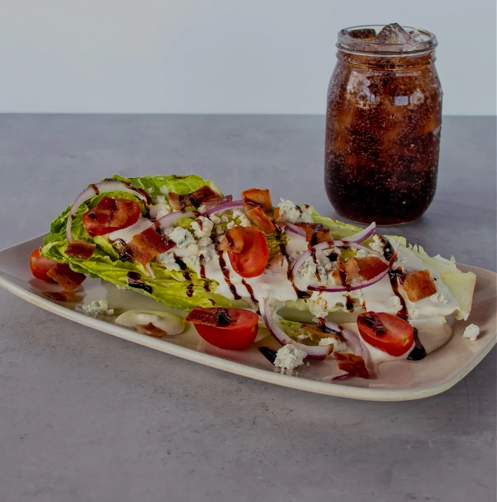 Wedge salad with blue cheese, bacon, tomatoes, onion, and a soda.