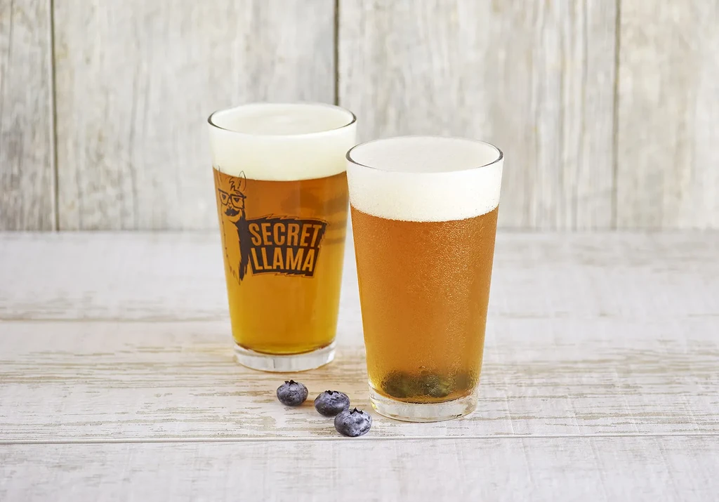 Two amber drinks on wood, one llama, other with blueberries.