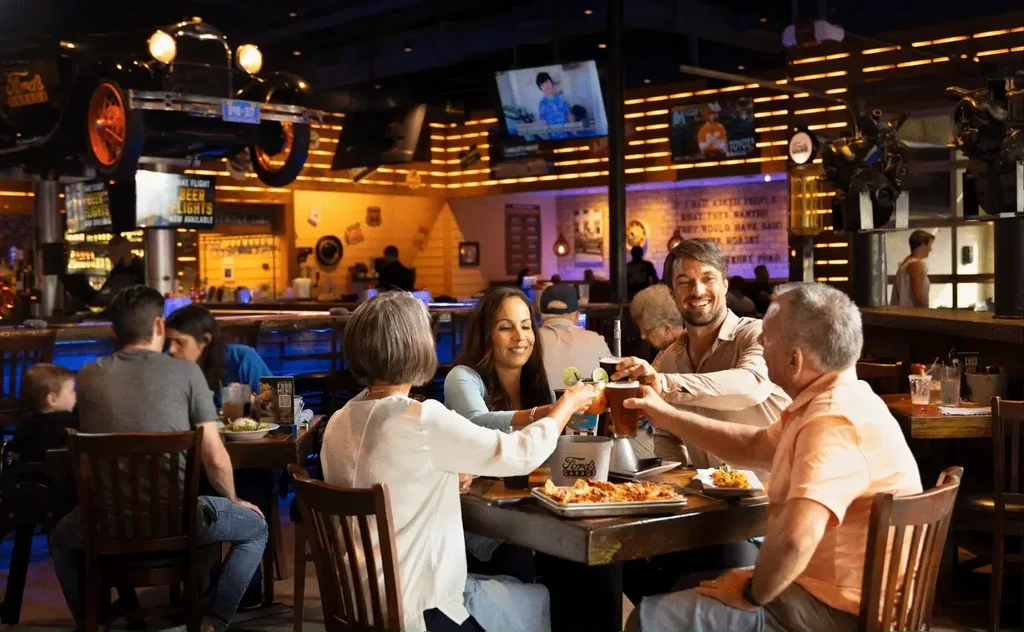 Four adults toast in a lively automotive-themed restaurant interior.