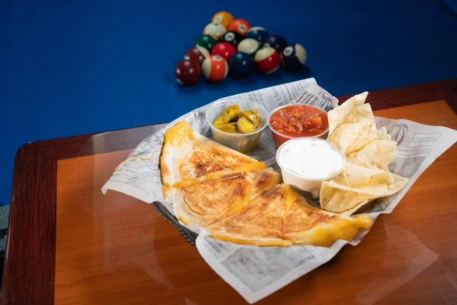 Quesadilla basket with chips, dips, near a pool table.