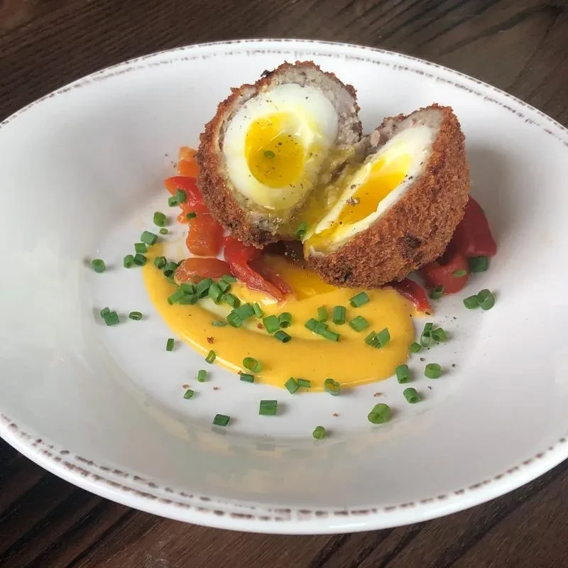 Halved Scotch egg with runny yolk, yellow sauce, and green chives.