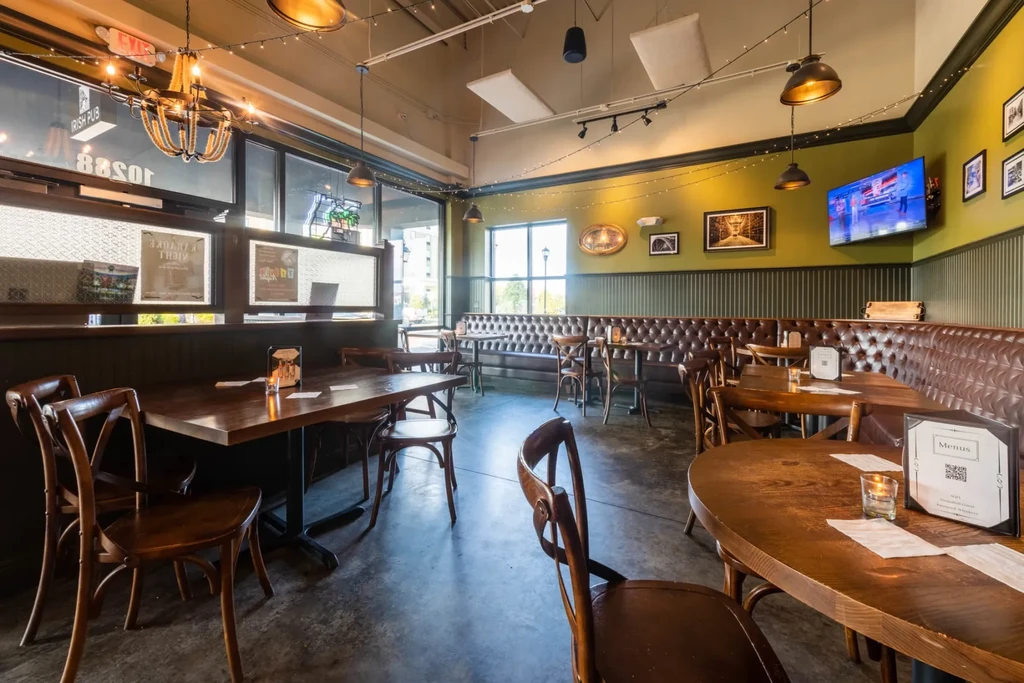Empty modern Irish pub with olive walls, leather booth, and string lights.
