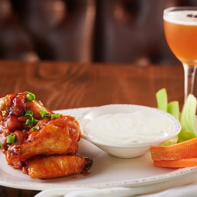 Glossy chicken wings, creamy dip, celery, carrots, and an amber drink.