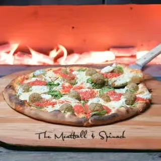 Wood-fired meatball and spinach pizza on a paddle, oven glowing.