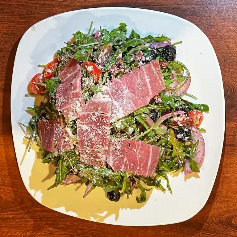 Gourmet salad with prosciutto, dark greens, tomatoes, nuts, and Parmesan.
