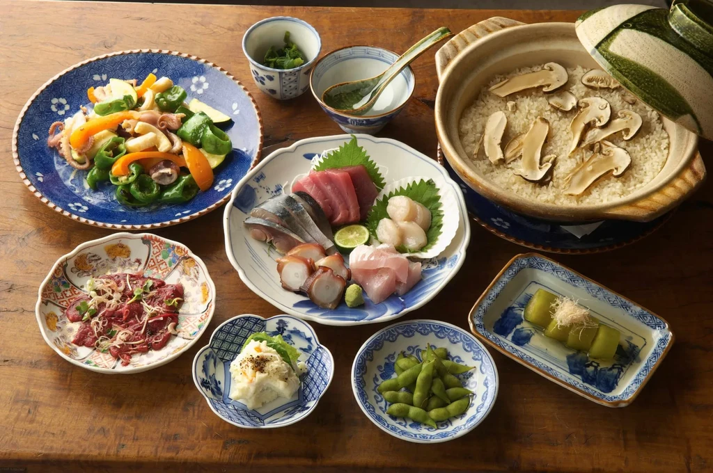 Assorted Japanese dishes, including sashimi, rice, and vegetables, on a wooden table.