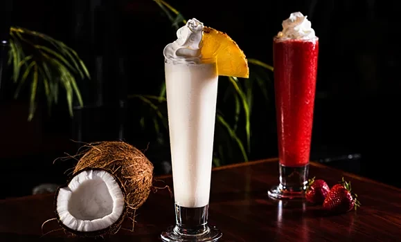 Two blended tropical drinks: coconut with pineapple, strawberry slush.