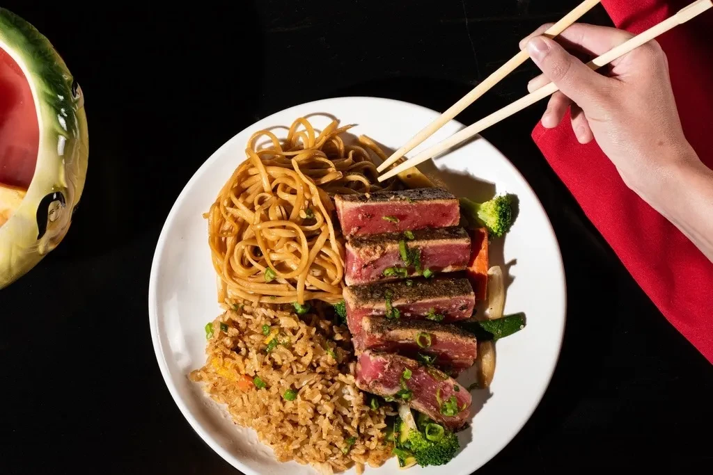 Seared tuna, lo mein, fried rice, and vegetables with chopsticks.
