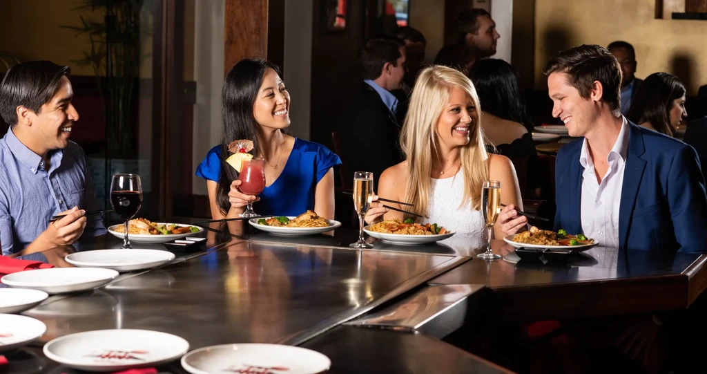 Four smiling people dining together at a lively restaurant table.