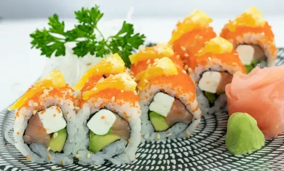 Plate of inside-out sushi rolls with fruit topping, ginger, and wasabi.