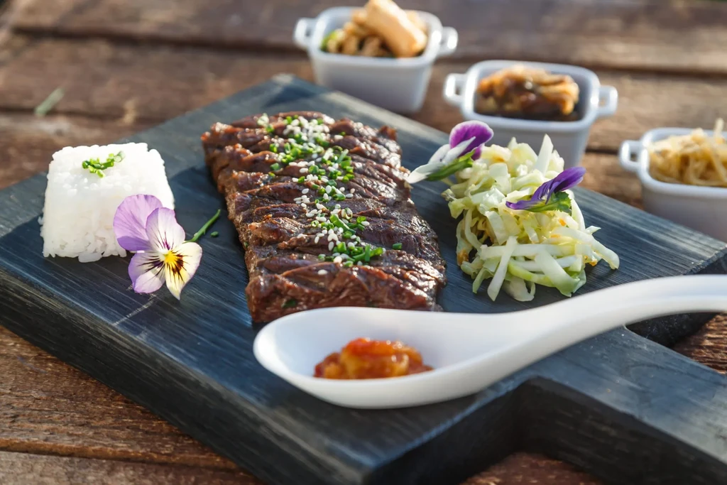 Sliced grilled meat, rice, cabbage, and sauce on a rustic board.