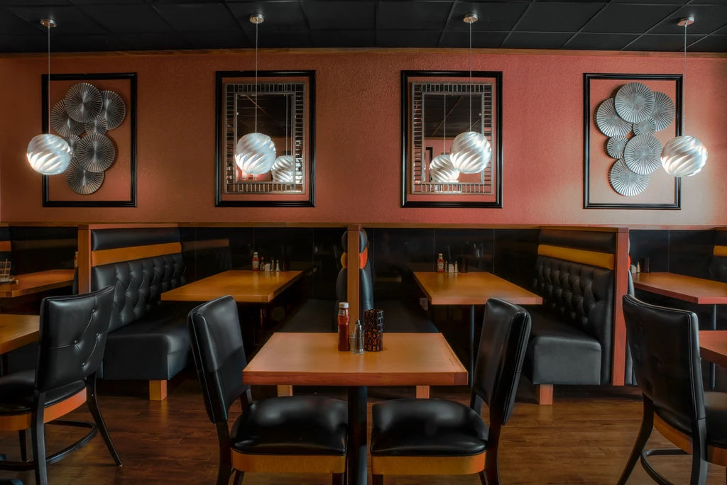 Warm restaurant interior with black booths, light wood tables, modern decor.