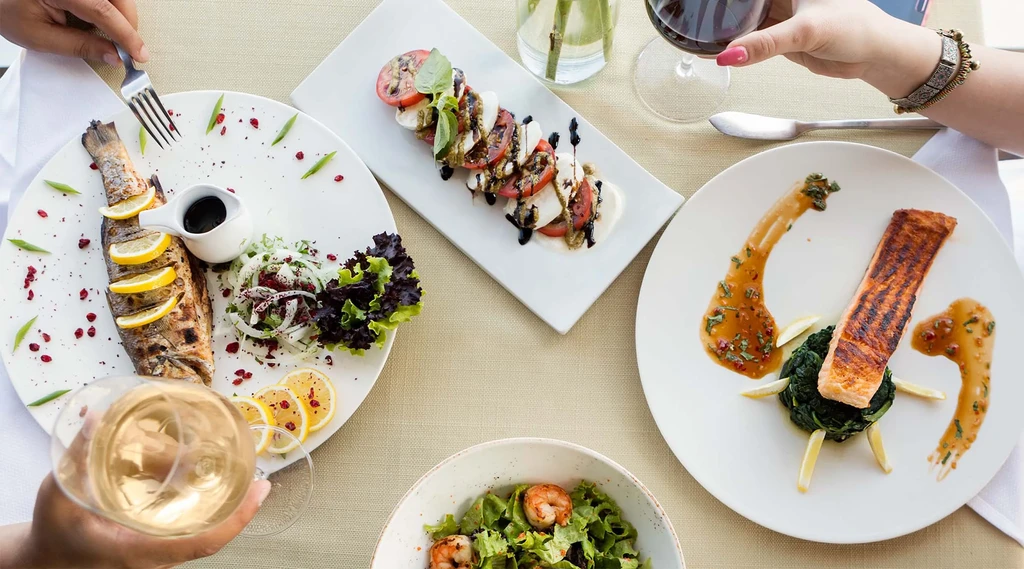 Overhead table view with multiple seafood dishes, salads, and hands dining.