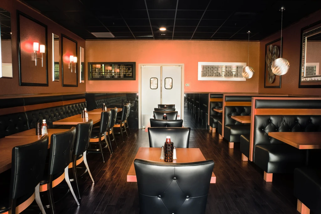 Empty restaurant interior with black booths, wood tables, and terracotta walls.