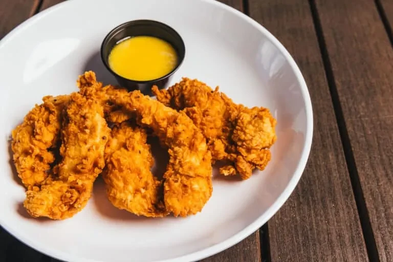 Crispy fried chicken tenders with yellow dipping sauce on a wooden table.