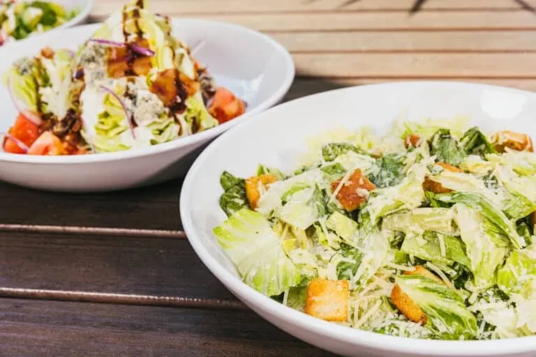 Caesar salad foreground, wedge salad background, on a wooden table.