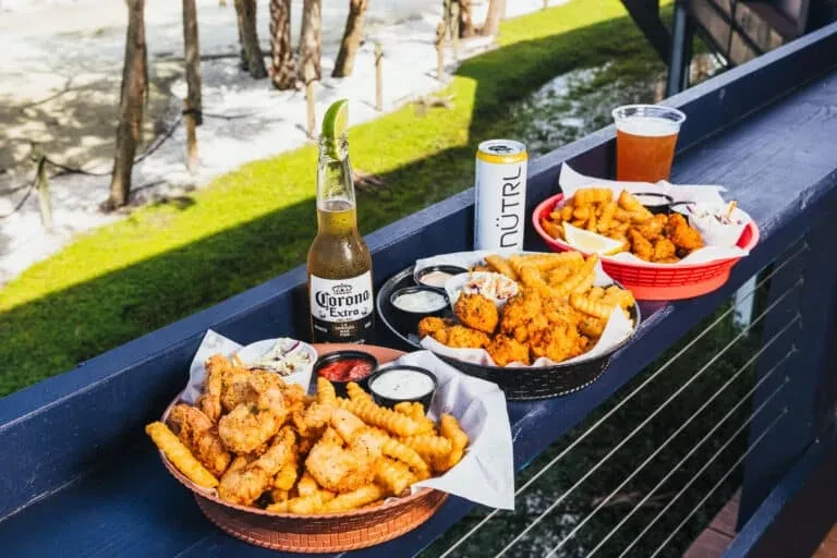 Fried seafood, fries, beer, and seltzer on an outdoor railing.