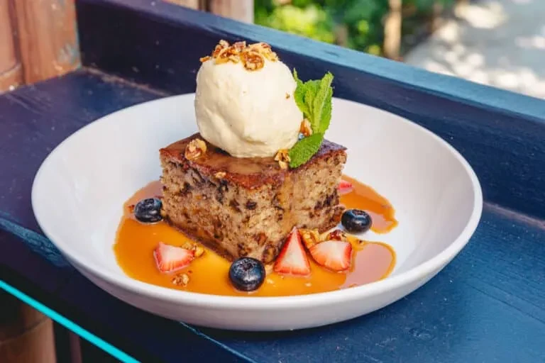 Square cake with ice cream, mint, berries, nuts, and caramel sauce.