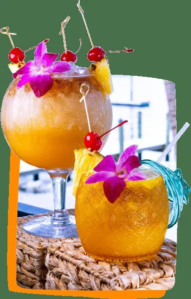 Two brightly colored, elaborately garnished cocktails on a woven mat.