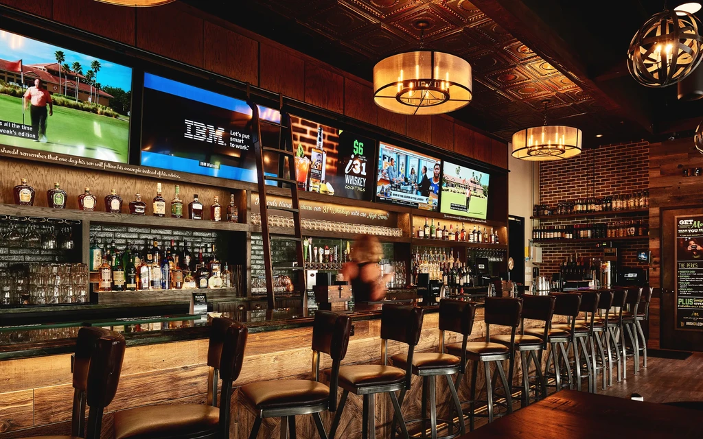Upscale, rustic bar interior with wooden counter, liquor displays, and televisions.